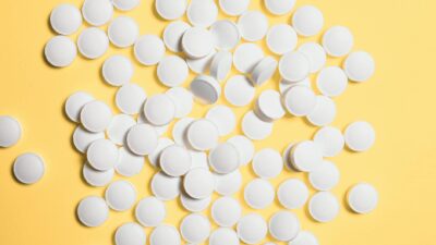 Scattered white pills on a vibrant yellow background, symbolizing healthcare and medicine.