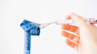 A floral-handled fork twirls a blue measuring tape, symbolizing diet and health.
