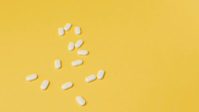 From above of small white ellipse shaped pills of same size randomly placed on bright yellow background