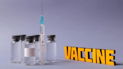 Syringe and vaccine vials with 'vaccine' text on a gray background, representing vaccination efforts.