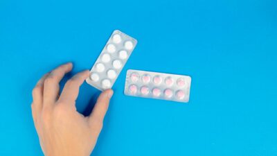 Image of a hand reaching for blister packs against a blue background, offering copy space.