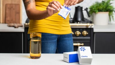 Close-up of person opening supplement sachet in modern kitchen setting.