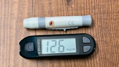 A digital glucometer displaying 126 mg/dL with a lancing device placed on a wooden surface.