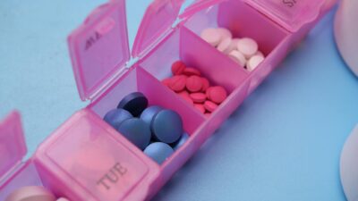 Pink pill organizer with colorful tablets arranged for weekly medication management.