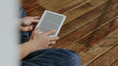 Close-up of hands holding an e-reader on a wooden floor, depicting a casual reading moment.