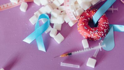 Creative composition highlighting diabetes awareness with donut, syringe, and sugar cubes on purple background.