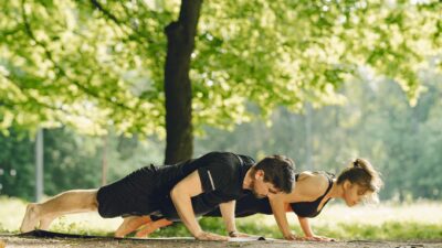 Fit couple doing push-ups in a sunny park, embracing outdoor fitness and healthy living.
