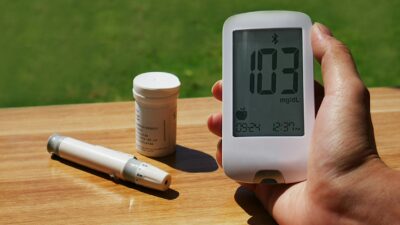 Blood glucose monitor displaying 103 mg/dL outdoors, emphasizing diabetes care.