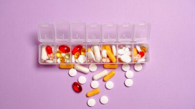 A daily pill organizer filled with various pills and capsules on a purple background. Ideal for healthcare topics.