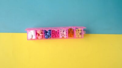 A vibrant photo of assorted pills in a pink organizer on a blue and yellow background, ideal for health topics.