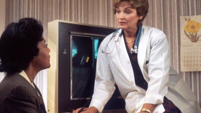 doctor sitting on desk talking to sitting woman