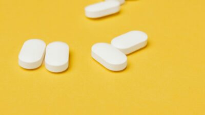 Set of medical white ellipse shaped pills placed in disorder on bright yellow background