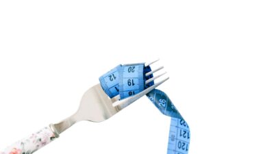 A fork entwined with a blue measuring tape, symbolizing dieting and weight management.