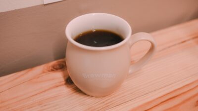 A mug of dark coffee sits on a wooden surface.
