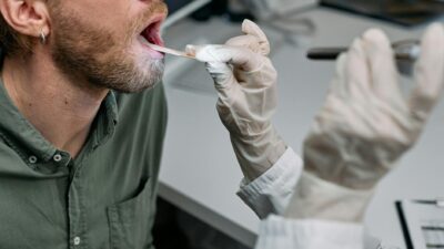 Close-up of a doctor examining a patient's throat with a tongue depressor in a clinical setting.