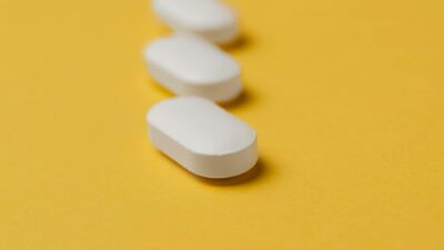 Closeup set of white elliptical medical pills arranged in row on bright yellow plain background