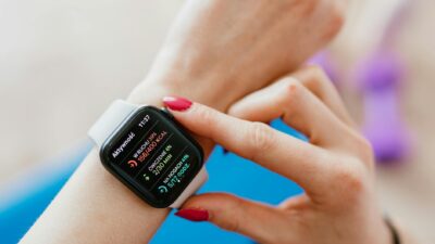 Unrecognizable female with manicure checking smartwatch on hand while sitting on yoga mat