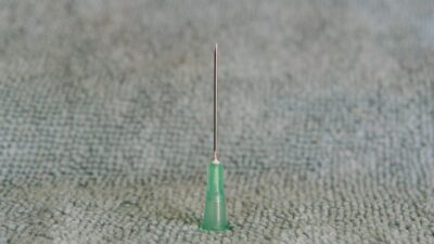 Close-up of a sharp medical needle with a green hub on a soft textured surface.