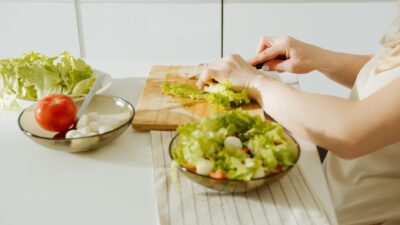 Enjoy healthy food preparation with fresh lettuce, tomato, and hands cutting on a wooden board.