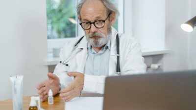 An elderly doctor in a white coat conducting an online medical consultation, focusing attentively.