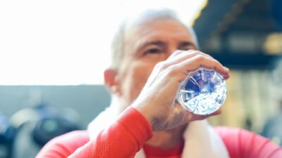 Elderly man in red shirt sipping water during gym session.