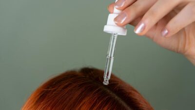 Close-up of applying serum to roots with a precision dropper on red hair, showcasing hair care routine.