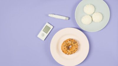 Top view of diabetes management concept with glucometer, insulin pen, and sweets on colorful plates.