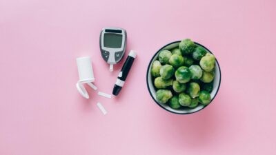 Top view of a glucometer and fresh Brussels sprouts on a pink background promoting health.