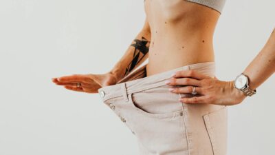 Close-up of a woman in oversized pants showcasing weight loss progress. Studio shot with neutral background.