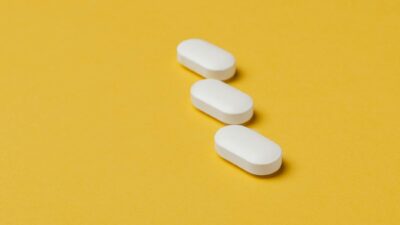 From above of white elliptical pills placed diagonally on bright yellow surface