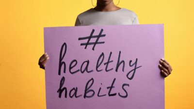 A photo of an adult woman holding a purple sign promoting healthy habits against a vibrant yellow background.
