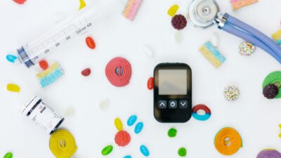 Flat lay of diabetes management tools and colorful candies on white background.