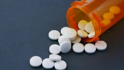Close-up of white pills scattered from an orange prescription bottle on a gray surface.