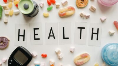 Creative flat lay with sweets around a 'HEALTH' text and monitoring device, symbolizing diabetes awareness.