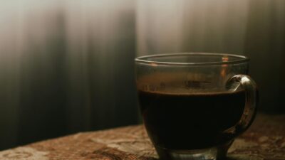 A tranquil scene featuring a glass cup of black coffee on a patterned cloth in soft window light.