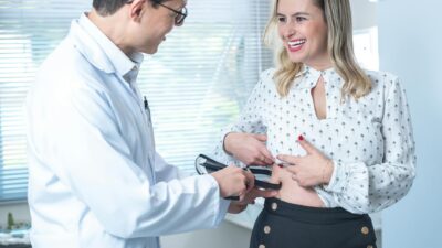 Healthcare professional using body fat caliper on a smiling woman during check-up.