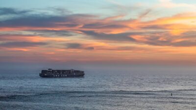 A container ship sails the ocean under vibrant sunset skies, evoking serene maritime travel.