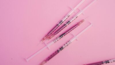 From above of syringes with needles filled with purple substance placed on pink background