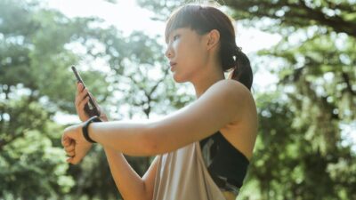 From above of young ethnic female in sportswear using smartphone and smart watch for restoring after exercising