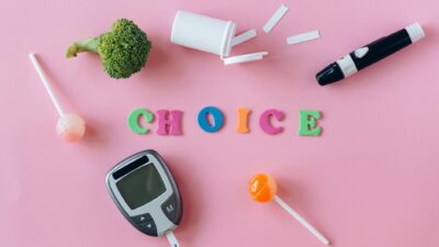 Artistic depiction of choosing between healthy food and sweets with glucose monitor on pink background.