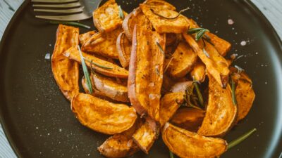 Close-up of crispy sweet potato wedges topped with rosemary, perfect for a healthy snack.