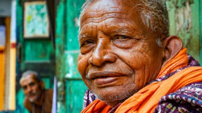Close-up portrait of an elderly man smiling in a colorful urban street setting.
