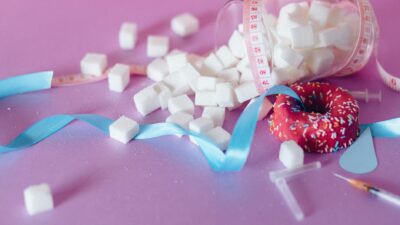 Creative representation of sugar consumption using cubes, donut, ribbon, and syringe.