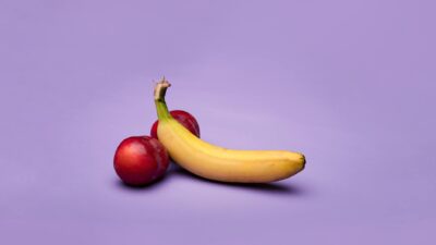 A vibrant image of a ripe banana and peaches on a purple backdrop, showcasing fresh produce.