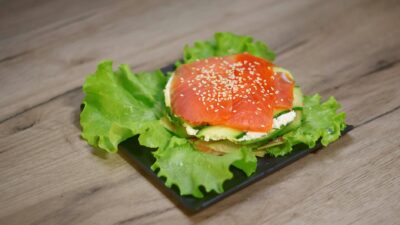 Fresh smoked salmon sandwich on lettuce and avocado, sprinkled with sesame seeds.