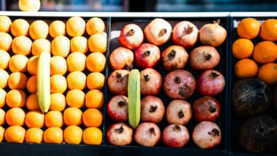 Colorful rows of fresh fruits including oranges, pomegranates, and bananas at a market.