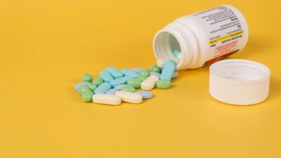Various pills spill from a bottle onto a vibrant yellow surface, highlighting health themes.