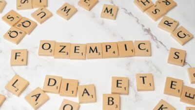 Scrabble tiles spelling Ozempic and diabetes on a marble surface.