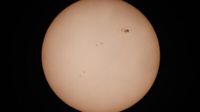 A detailed photograph of the sun highlighting visible sunspots against a dark background.