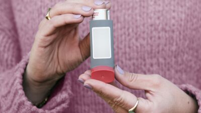 Female hands holding an asthma inhaler with a pink sweater background.